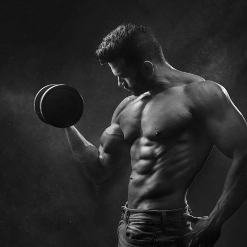 Powerful black and white portrait of a shirtless bodybuilder lifting dumbbells in the gym.