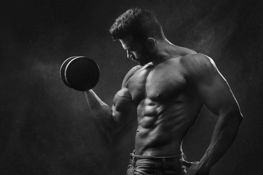 Powerful black and white portrait of a shirtless bodybuilder lifting dumbbells in the gym.