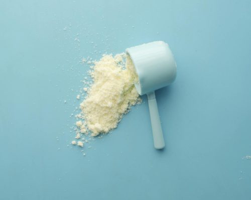 White powder spilled from a scoop on bright blue background. Clean and minimalistic food photo.