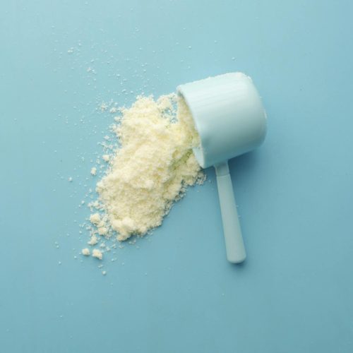 White powder spilled from a scoop on bright blue background. Clean and minimalistic food photo.