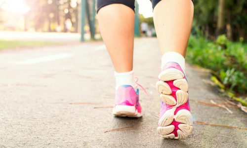 Close-up of a woman walking on a path in pink sneakers, embracing fitness and an active lifestyle.