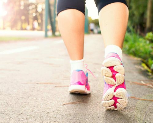 Close-up of a woman walking on a path in pink sneakers, embracing fitness and an active lifestyle.