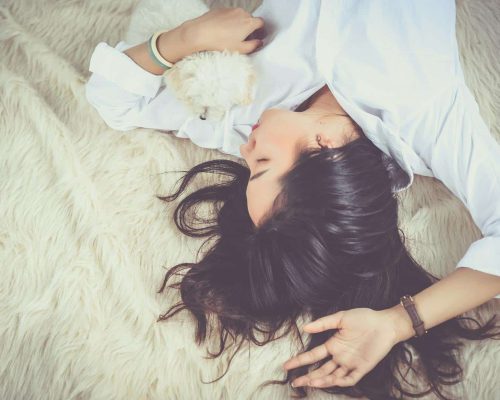 A woman peacefully sleeping with her pet dog on a soft, furry rug indoors.