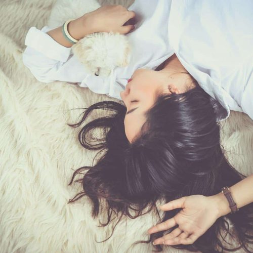 A woman peacefully sleeping with her pet dog on a soft, furry rug indoors.