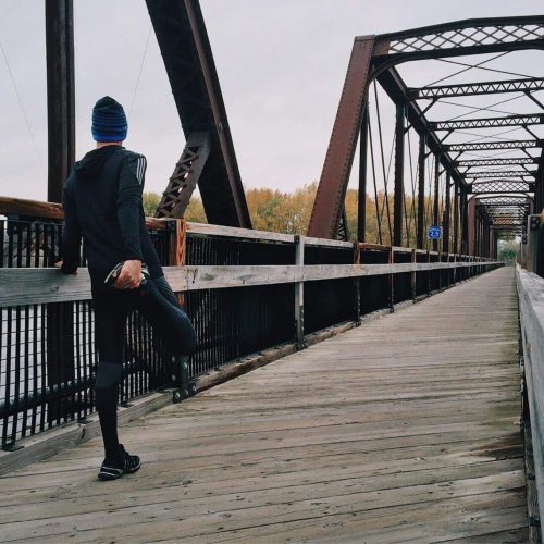 Man stretching on a wooden footbridge during a daytime run on an iron bridge, emphasizing fitness and recreation.
