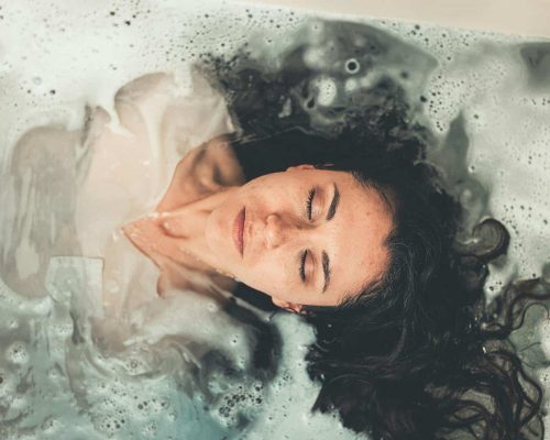 Woman with long hair enjoying a peaceful bubble bath with eyes closed, illustrating relaxation.