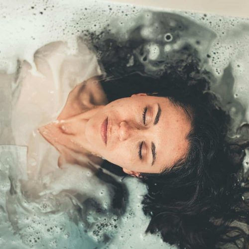 Woman with long hair enjoying a peaceful bubble bath with eyes closed, illustrating relaxation.