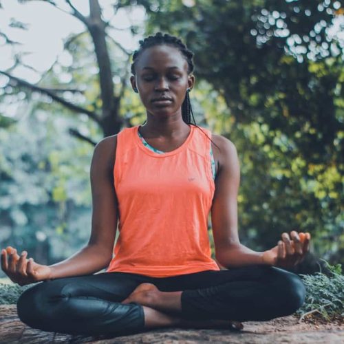 A woman meditating peacefully outdoors in a lush green setting, promoting relaxation and mindfulness.