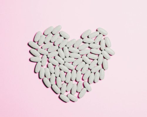 Artistic heart shape made from white pills on a pink background symbolizing love and healthcare.