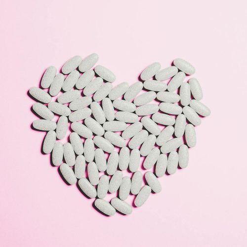 Artistic heart shape made from white pills on a pink background symbolizing love and healthcare.