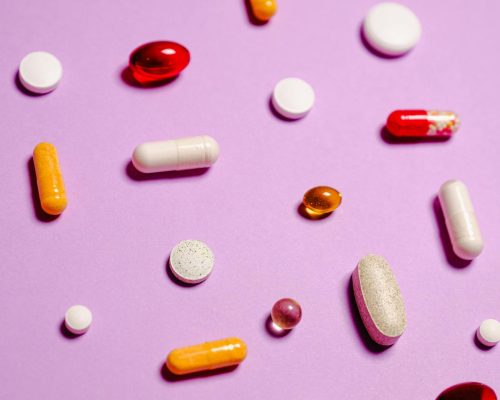 Various colorful pills and capsules scattered on a purple surface, representing healthcare and medication.