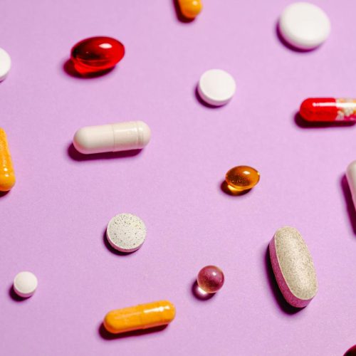 Various colorful pills and capsules scattered on a purple surface, representing healthcare and medication.