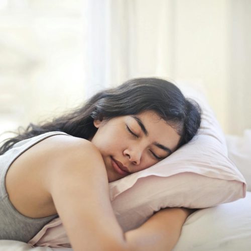 Serene woman resting on a comfortable bed with soft pillows and natural light.