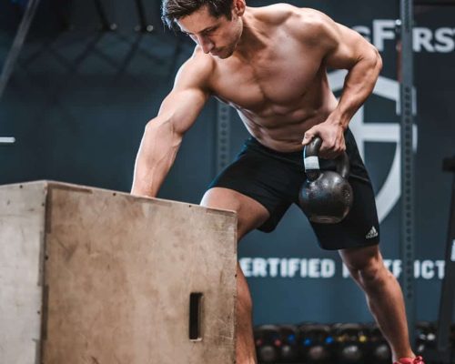Athletic man working out with a kettlebell, showcasing strength and fitness indoors.