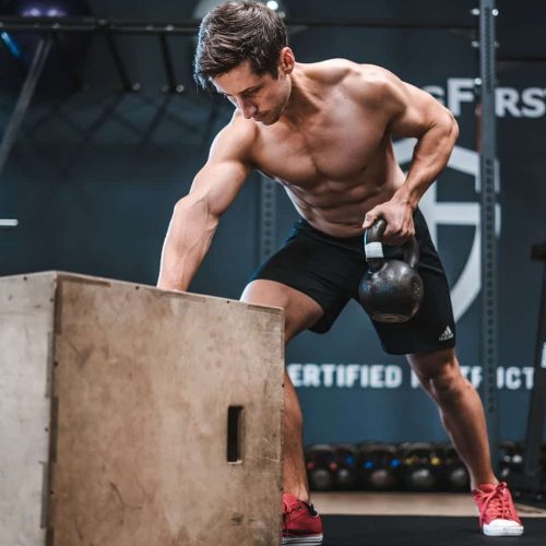 Athletic man working out with a kettlebell, showcasing strength and fitness indoors.