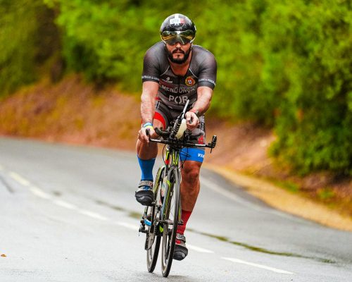 A focused cyclist racing on a road surrounded by lush greenery during summer.