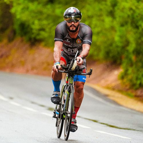 A focused cyclist racing on a road surrounded by lush greenery during summer.