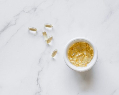 Top view of scattered capsules and a bowl on a marble surface, minimalistic setup.