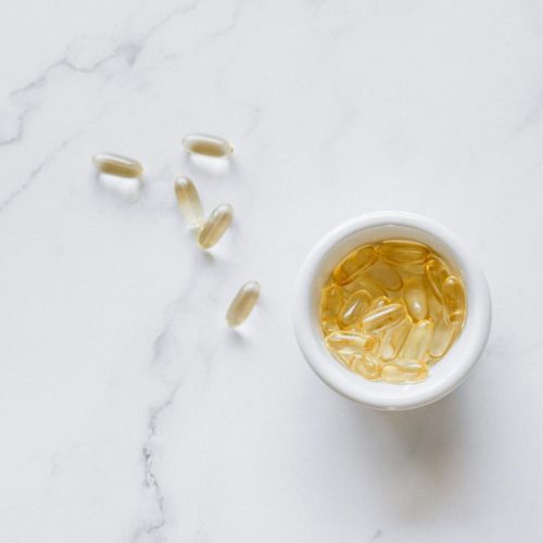 Top view of scattered capsules and a bowl on a marble surface, minimalistic setup.