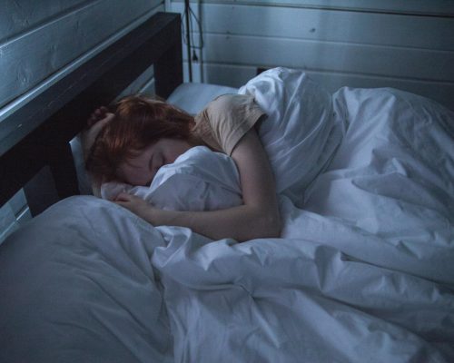A woman sleeping peacefully in a cozy bedroom, enveloped by soft white sheets, under the gentle glow of night lighting.