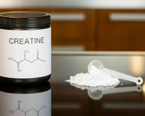 a bottle of creatine next to a spoon on a table